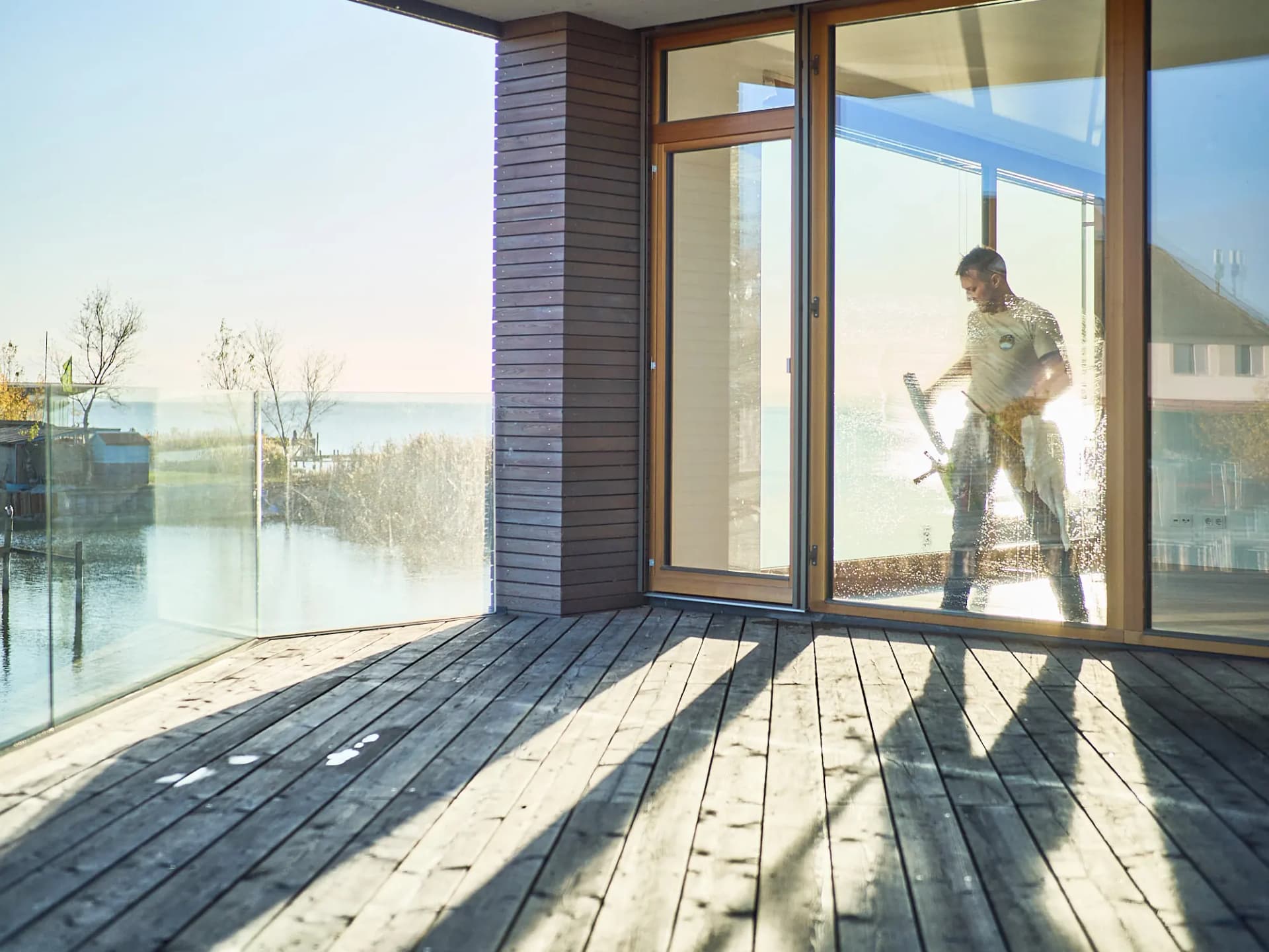 Morning sun through an open glass door onto a wooden terrace by the water
