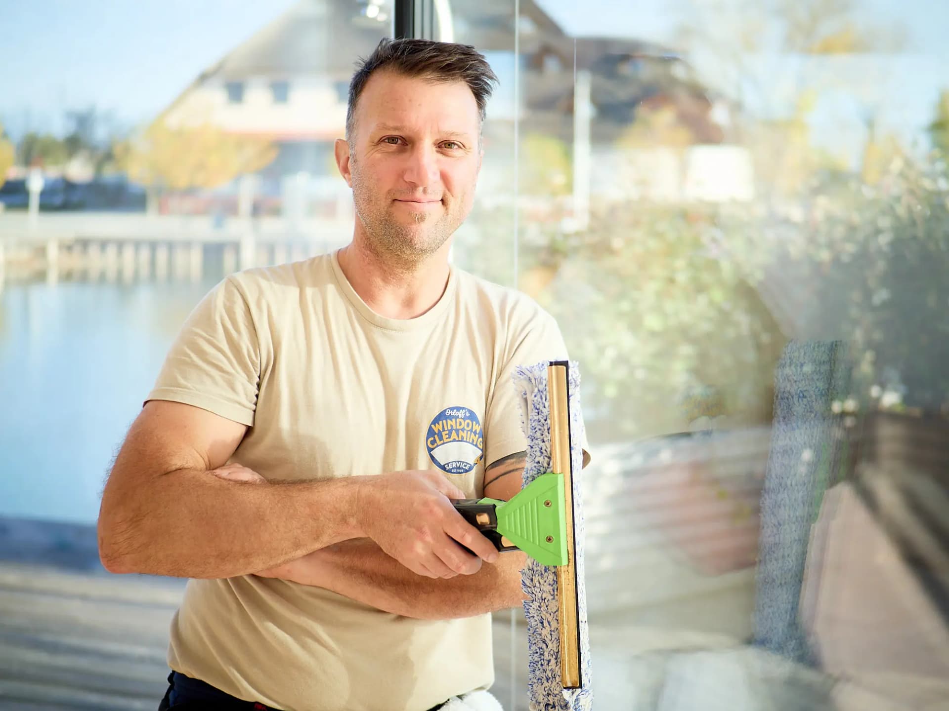 Justin Orloff smiling, arms crossed, a squeegee in his hand, water behind him