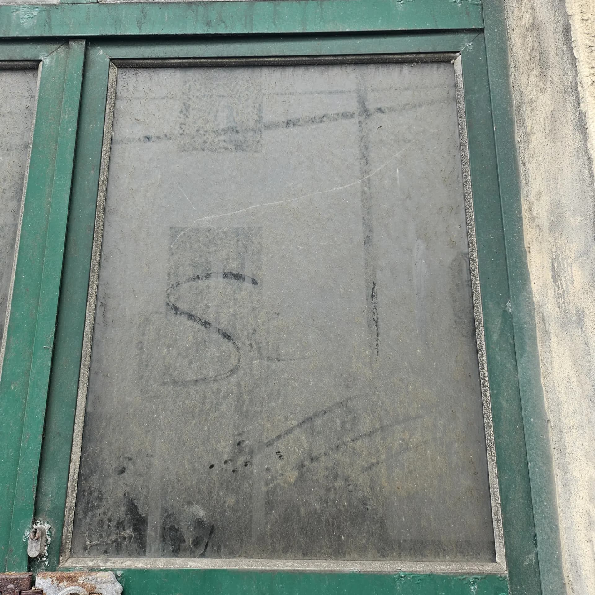 An old green window frame, the glass grey with years of grime and marks drawn in the dirt