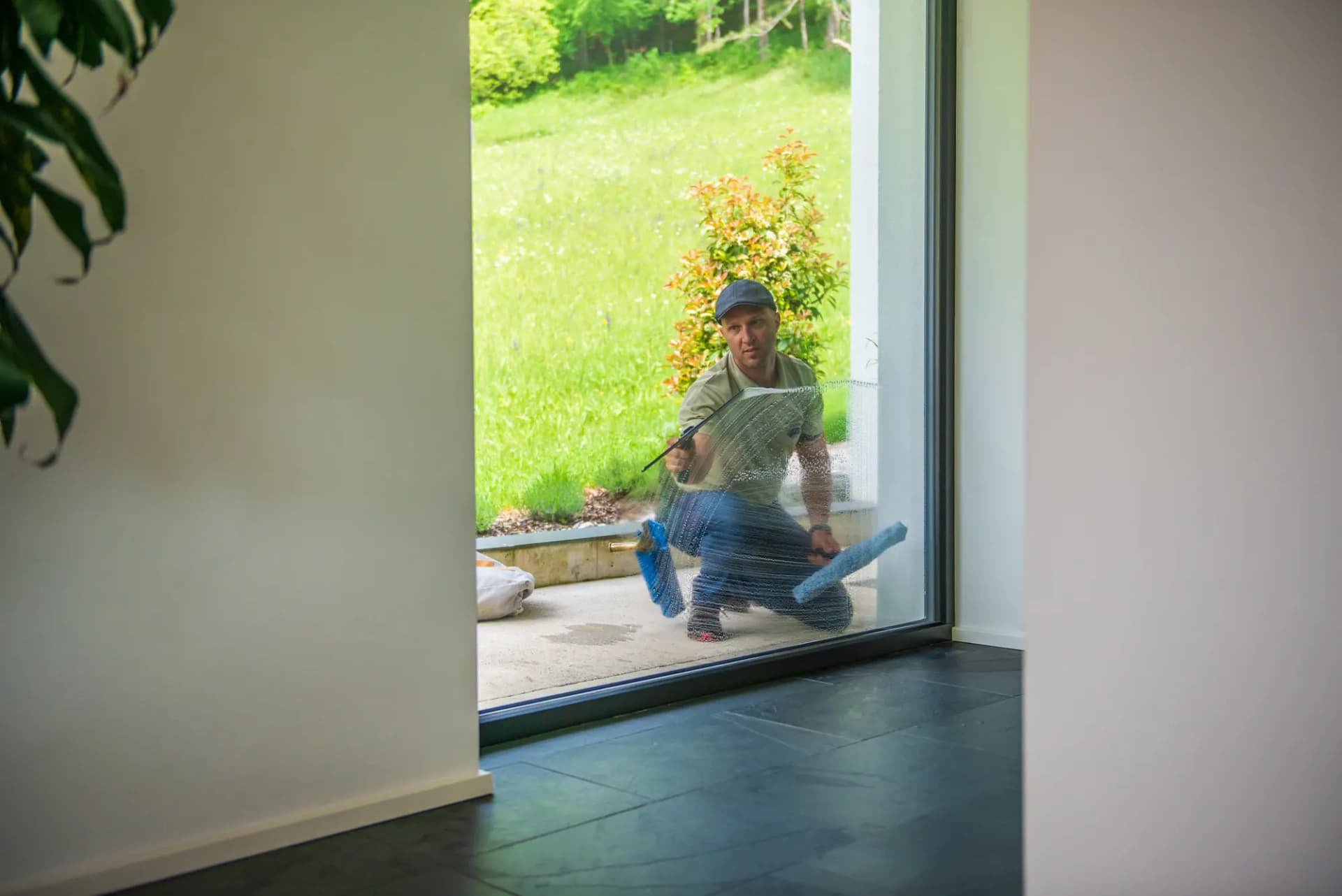 Seen from inside an empty room: Justin kneeling outside the glass, cleaning the window alone