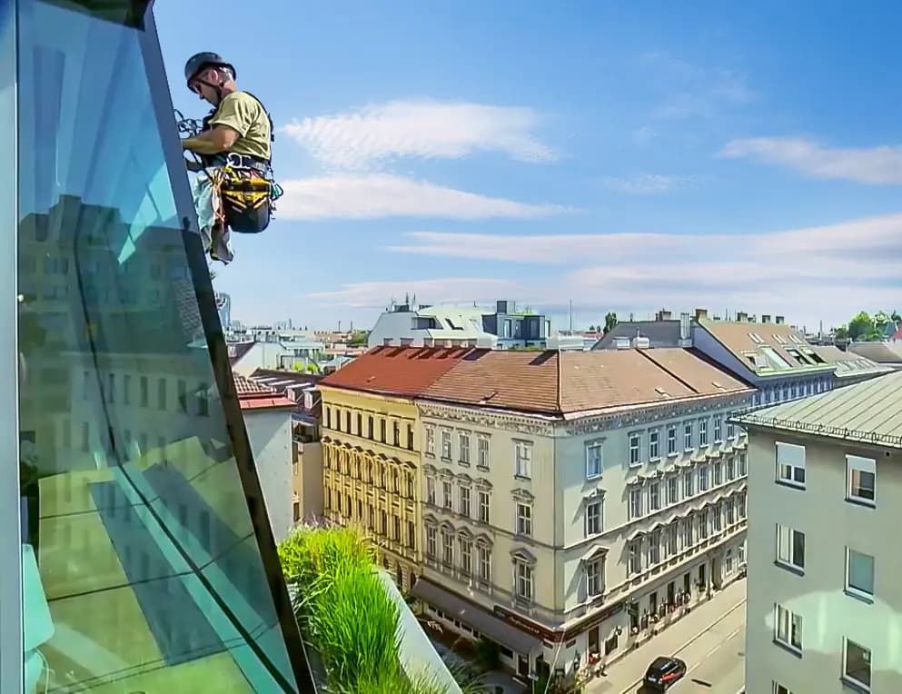 Justin on a rope beside a glass facade, high above the rooftops of Vienna