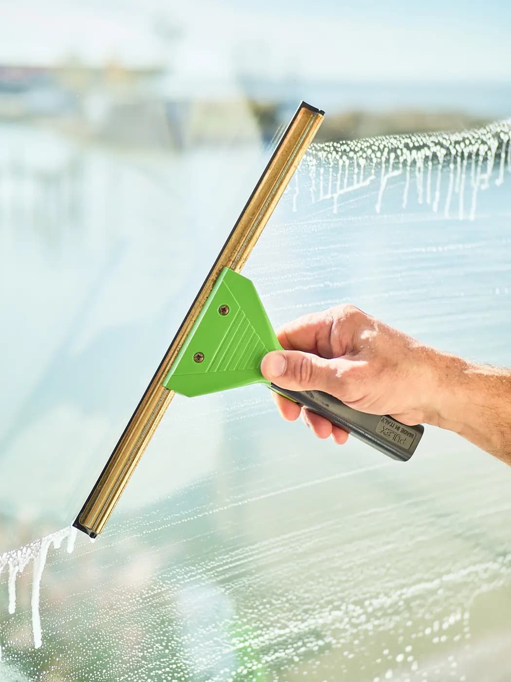 A squeegee pulling a clean line through soap water, a harbour behind the glass
