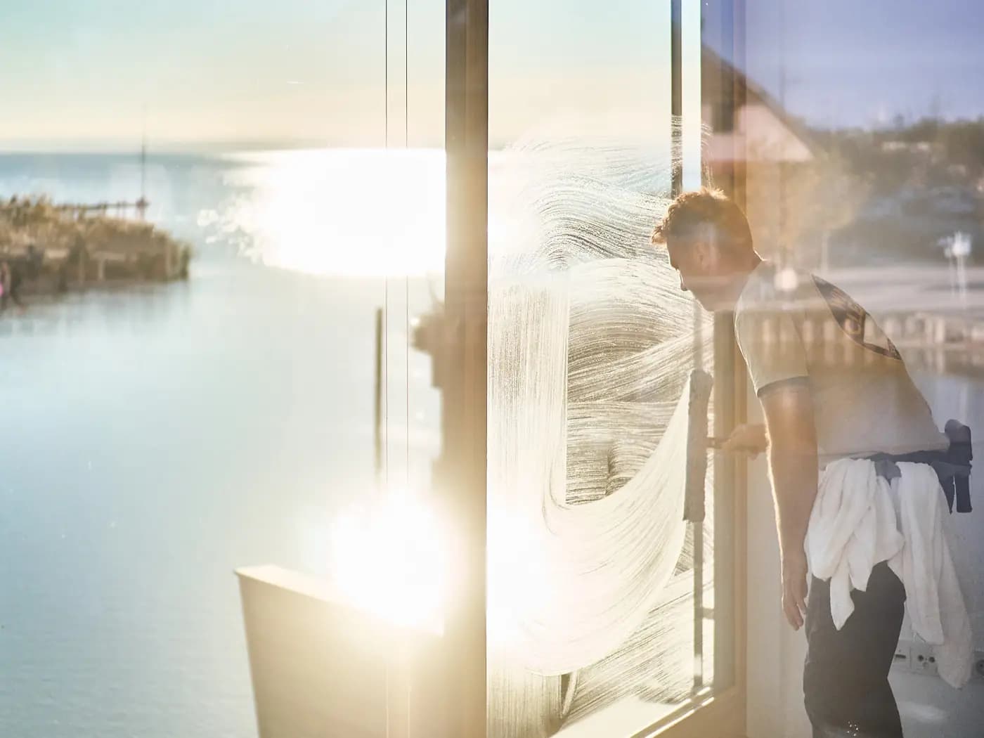 Justin washing a sunlit window by the water, soap swirls catching the light